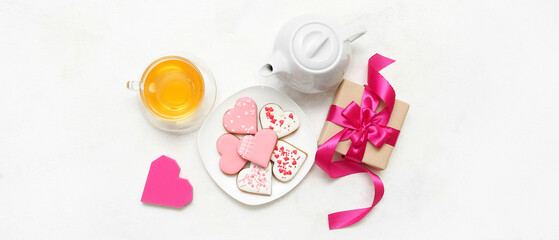 Plate with tasty heart shaped cookies, gift and hot tea on light background. Valentine's Day celebration