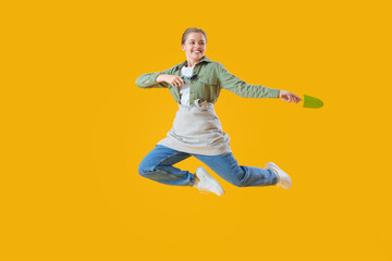 Fototapeta na wymiar Female gardener with tools jumping on yellow background
