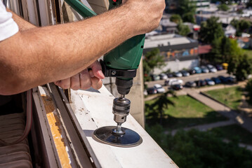 Machine during sanding rust from an old window sill with a parking and a park of a residential city quarter in a background