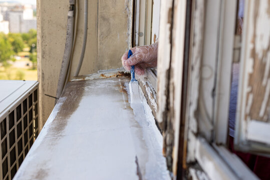 Hand holding a brush while painting an old window cill in white