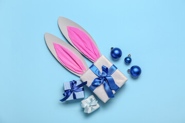 Paper bunny ears with Christmas balls and gifts on blue background