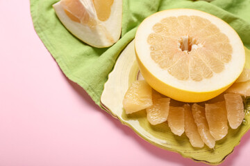 Plate with pomelo fruit and slices on pink background, closeup