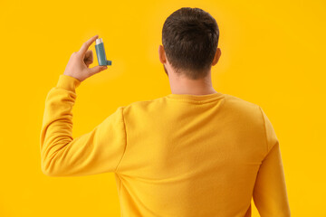 Man with inhaler on yellow background, back view