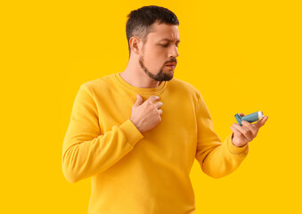 Sick man with inhaler on yellow background