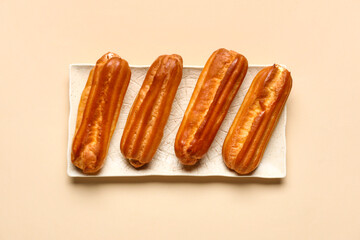 Plate with sweet eclairs on color background