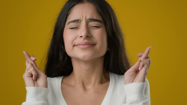 Indian girl lady in yellow studio background crossed fingers close eyes praying hope wish woman waiting miracle pray ask God for help success luck believe trust expect win beg winning dreamy wishing