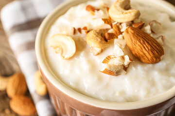 Bowl with delicious rice pudding, cashew and almond nuts on wooden table, closeup