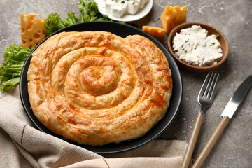 Plate with delicious cheese pie, lettuce and ingredients on grey table