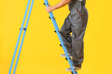 Male worker with ladder on yellow background