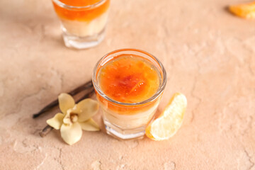 Shot of delicious pudding with jam, vanilla sticks and tangerine segment on beige table