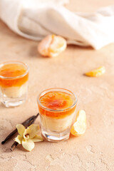 Shots of delicious pudding with jam, vanilla sticks and tangerine segment on beige table