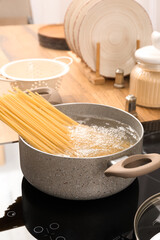 Cooking pot with raw pasta and boiling water on electric stove in kitchen