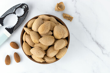 Almonds in a wooden bowl and a nutcracker on a marble background. Top view. selective focus