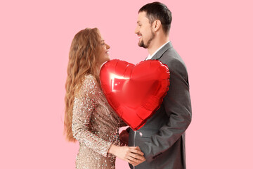 Fototapeta na wymiar Happy young couple with heart-shaped balloon on pink background. Valentine's Day celebration