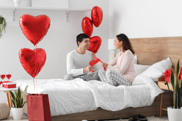 Young couple with paper hearts in bedroom on Valentine's Day