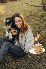 Beautiful caucasian woman celebrates her dog's Birthday smiling and holding the cake with a burning candle. Miniature schnauzer breed 
