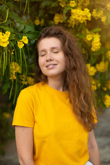 Portrait of happy beautiful bearded girl, young positive woman with beard is smelling beautiful yellow flowers in the garden, smiling, enjoying spring or summer day, breathing deep deeply fresh air