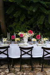 Flowers decorations on the table. Beautiful plates and candles.  Table setting by the pink, yellow. white flowers outdoor.
