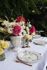 Flowers decorations on the table. Beautiful plates and candles.  Table setting by the pink, yellow. white flowers outdoor.