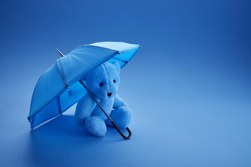Blue teddy bear with umbrella on blue background. Blue monday concept.