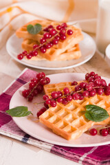 Waffle with red currant and honey on white dish.