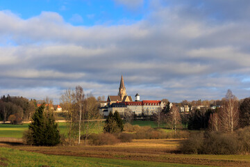 View over fields and bushes to the towers of the Archabbey St. Ottilien in Bavaria with cloudy sky