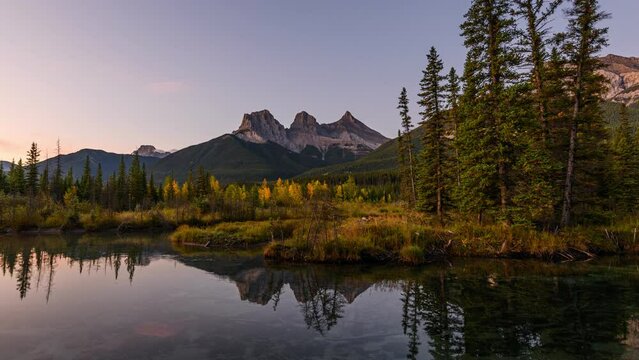 Sunrise over Three Sisters mountains in autumn forest reflection on pond at Canmore