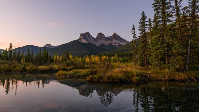 Sunrise over Three Sisters mountains in autumn forest reflection on pond at Canmore