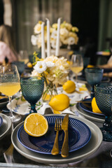Table setting with blue plates, glasses, golden cutlery, lemons, candles and different flowers. Ladies party outdoor