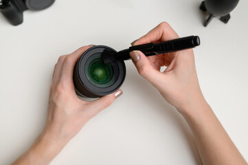 Hands cleaning the lens of a digital camera from dust with a special cleaning brush. The concept of care for photographic equipment, cleaning the camera lens.