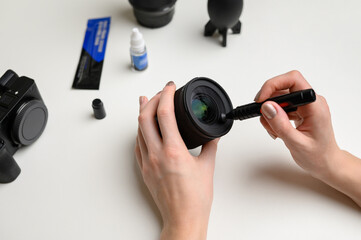 Hands cleaning the lens of a digital camera from dust with a special cleaning brush. The concept of care for photographic equipment, cleaning the camera lens.