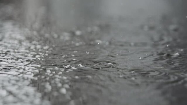 Slow motion closeup of summer rain falling into big puddle on asphalt