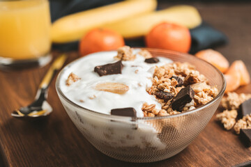 Granola cereal oatmeal with white yogurt, chocolate, banana fruit and nuts in a bowl on dark wooden...