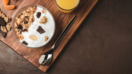 Granola cereal oatmeal with white yogurt, chocolate, fruist and nuts in a bowl on dark wooden board, top view