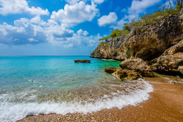 Tropical Caribbean island beach with turquoise waves crashing on brown sand beach in Curacao.