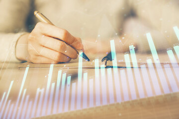 Hands writing information about stock market in notepad. Forex chart holograms in front. Concept of research. Multi exposure
