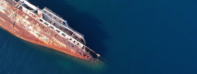 Aerial top down ultra wide photo of capsized abandoned passenger ship wreck left to rust near shore