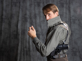 A lawyer with a pistol in a holster, gray shirt and trousers with suspenders, retro style. A young...