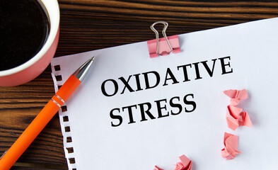OXIDATIVE STRESS - words on a white sheet on a wooden brown background with a cup of coffee and a...