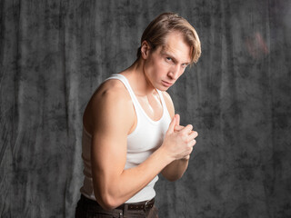 A sporty and athletic guy in a white T-shirt, boxing. A young man in a vintage outfit, posing in a studio on gray