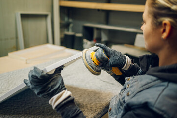 Woman carpenter using an electric sander in a workshop or factory