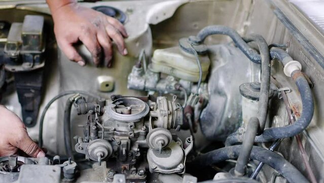 Hands of Auto mechanic to repairing and maintenance the old car in the fuel carburetor system.