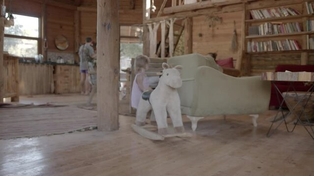 Child is playing in a large wooden house. Toddler is sitting on a toy horse