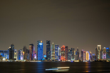 Obraz premium Banner of capital city of Qatar by night. Doha West Bay skyline mirroring in Doha Bay. Panorama of glassed skyscrapers of Doha, Qatar, Middle East, Arabian Peninsula in Persian Gulf. Night urban scene