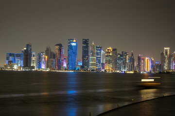 Naklejka premium Banner of capital city of Qatar by night. Doha West Bay skyline mirroring in Doha Bay. Panorama of glassed skyscrapers of Doha, Qatar, Middle East, Arabian Peninsula in Persian Gulf. Night urban scene