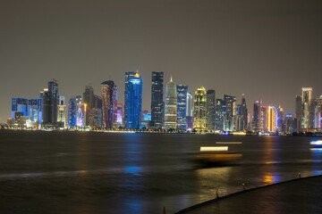 Banner of capital city of Qatar by night. Doha West Bay skyline mirroring in Doha Bay. Panorama of glassed skyscrapers of Doha, Qatar, Middle East, Arabian Peninsula in Persian Gulf. Night urban scene