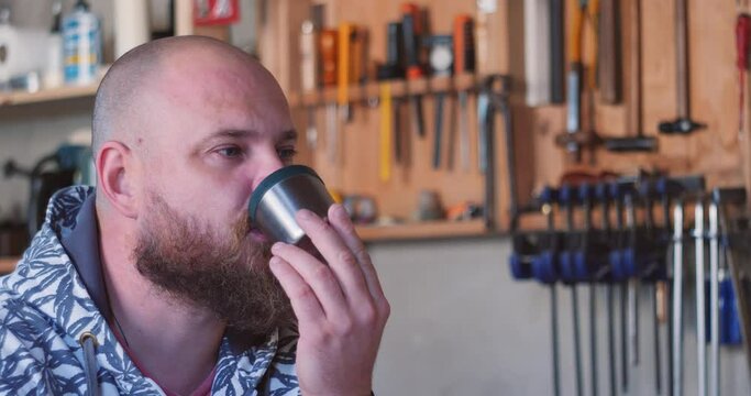 Carpenter in the workshop drinks tea with a sandwich against the background of a hand tool