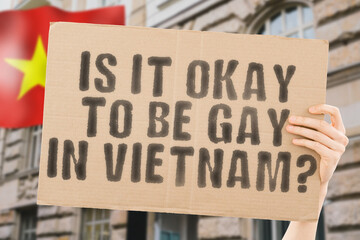 The question " Is it okay to be gay in Vietnam? " is on a banner in men's hands with blurred background. Friendly. Passionate. Contact. Date. Dating. Lover. Partner. Boyfriend. Pleasant. Approval