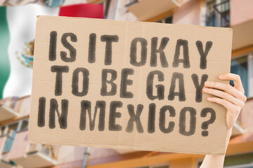 The question " Is it okay to be gay in Mexico? " is on a banner in men's hands with blurred background. Friendly. Passionate. Contact. Date. Dating. Lover. Partner. Boyfriend. Pleasant. Approval