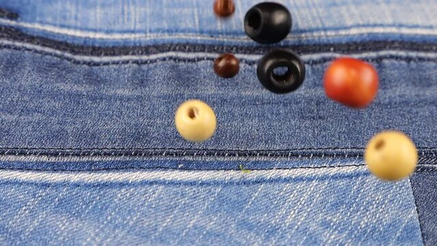 Decor elements made of natural materials, wood and shell beads fall on denim. Slow motion.